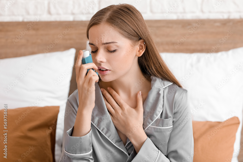 Sick young woman with inhaler in bed