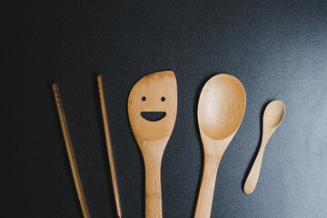 Set of wooden kitchen utensils, spoon, tongs and spatula on black table background.