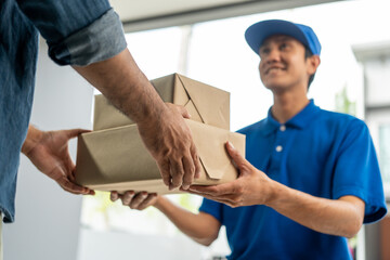 Asian delivery man with parcel in hand of blue uniform sending parcel to customer front of the house from shopping online with good service. Courier man send a package to destination.