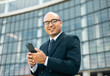 © Chanakon - Senior manager business man in suit with cell phone at the buildings downtown. Confident man using smartphone looking towards their goals for success. Executive business man