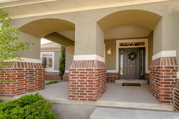 Wall Mural - Utah- Entrance of a house with wide gray front door with wreath, side lights and transom window. There are plants at the front of the house with painted gray and red bricks wall.