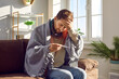 © Studio Romantic - Sick young man sitting on sofa and checking his temperature wrapped in blanket and touching his forehead with hand. Guy with seasonal flu or cold feel unhealthy with influenza at home.