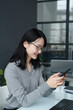 © AnnaStills - Young Asian businesswoman reading message on her smartphone and smiling while working at her workplace
