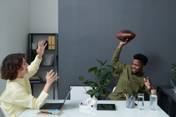 Two colleagues having fun during meeting at table, they playing rugby throwing ball to each other