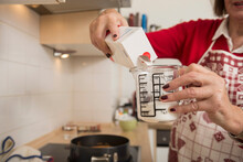 Senior woman filling icing sugar into a measuring cup in kitchen, Munich, Bavaria, Germany