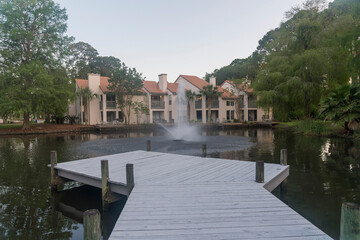 Wall Mural - Wooden deck above the decorative lake at the front of the townhouses in Destin, Florida. Views of the lake with water fountain at the front of the townhomes near the forest.