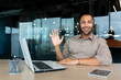 © Liubomir - Portrait of tech support and online customer service worker, man with video call headset smiling and looking at camera, african american man in shirt working inside office using laptop.