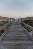 Fototapeta Przestrzenne - Vertical shot view of a wooden pathway with railings in between grassy sand dunes in Destin, Florida. Pathway heading to the beack with blue ocean under the horizon skyline.