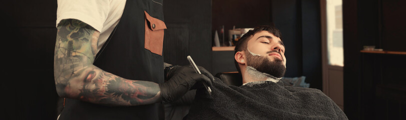 Wall Mural - Professional hairdresser working with bearded client in barbershop. Banner design