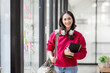 © David - Young curly Indian student Asian woman wearing backpack headphones holding books and tablet in office blue background.