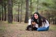 © Ladanifer - Young caucasian woman hugging her american staffordshire and french bulldog mixed breed dog and looking at camera at a pine forest.