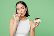 © ViDi Studio - Young happy fun woman wear white clothes holding in hand pice of cake dessert lick fingers isolated on plain pastel light green background. Proper nutrition healthy fast food unhealthy choice concept.