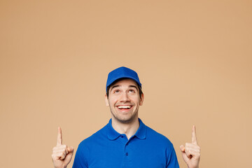 Wall Mural - Fun delivery guy employee man wearing blue cap t-shirt uniform workwear work as dealer courier point index finger overhead indicate on area isolated on plain light beige background. Service concept.