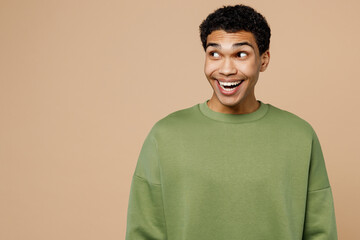 Wall Mural - Young surprised shocked fun cool man of African American ethnicity wear green sweatshirt look aside on area isolated on plain pastel light beige background studio portrait. People lifestyle concept.