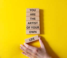 Wall Mural - Motivation symbol. Wooden blocks with words You are the artist of your own life. Businessman hand. Beautiful yellow background. Business and motivation concept. Copy space.