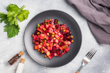 Vinaigrette with beetroot and boiled vegetables, traditional Russian homemade salad. A black plate on a light background.