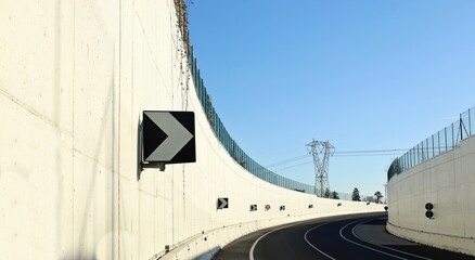 Road curve inside an underpass bordered with two high white concrete wall. Directional arrow signs on focus. Background for copy space.	