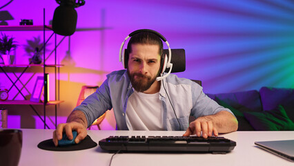 Gamer bearded guy, in a gaming headset, wins a video game. Cybersportsman in a neon room. Lifestyle gamer, online games. Victory in the E-Sport tournament