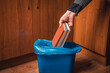 A man throws paper books into a trash can. Man's hand with old books and trash can in blue