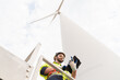 © amorn - Male engineer working with plan inspecting or maintenance of wind turbines at windmill field farm. Male engineer using computer tablet control or monitoring wind turbine system at wind turbines farm
