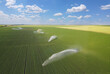 Aerial view of irrigation system rain gun sprinkler on agricultural soybean field helps to grow plants in the dry season. Drone shot of landscape rural scene beautiful sunny day, clouds and blue sky