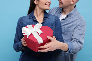 Wall Mural - Boyfriend presenting gift to his girlfriend on light blue background, closeup