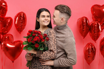 Wall Mural - Happy couple celebrating Valentine's day. Beloved woman holding bouquet of roses near heart shaped air balloons on red background