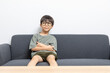 © bennnn - Cute Asian boy with eyeglasses looking up or right, sitting on a sofa at home. Curious kid thinking.