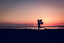 Boy Running With 2 Heart Balloons At The Beach At Sunset