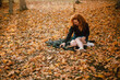 © Cavan Images - Happy young woman sitting on field with dry leaves during autumn