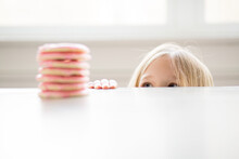 Blond Girl Peeking At Stack Of Pink Frosted Sugar Cookies On Table