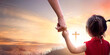 Child's hand hold father's finger on  cross on autumn sunset background