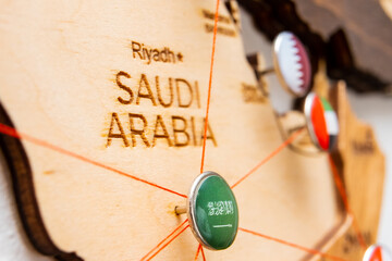 Wall Mural - Saudi Arabia flag on the pushpin and red threads on the wooden map. Travel or logistic routes. Influence in geopolitics and world economy. 