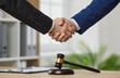 © Studio Romantic - Professional lawyer or legal advisor shaking hands with a client. Two men in suits exchange handshakes over an office desk with a judge's gavel. Close up of male hands. Law, legal services concept