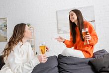 Happy Woman Holding Glass Of Beer While Pointing At Friend In Living Room