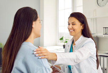 friendly smiling female doctor holding woman's shoulder telling her positive news about her health. 