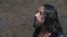 Close Up Wanderer Rejoices In The Long-awaited Rain In The Desert. An Emaciated Man With Long Dark Hair Stretches Out His Arms To The Sky As Raindrops Fall On Him. 200 Fps Slow Motion