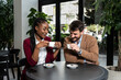© Srdjan - Young man and African American woman sitting in cafeteria drinking coffee flirting talking laughing and seducing outside working hours and colleague in restaurant away from busy street