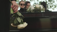 Midsection Of Unrecognizable Woman Holding Two White Roses While Standing By Wooden Coffin At Outdoor Funeral Ceremony