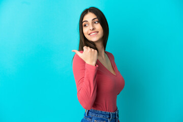 Wall Mural - Young caucasian woman isolated on blue background pointing to the side to present a product