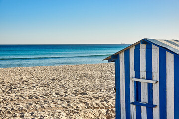 Beach house with blue and white stripes for storing beach furniture on an empty beach in front of the blue sea in Tunisia