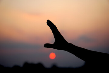 Wall Mural - silhouette of human hand raised to make a wish, sunset background