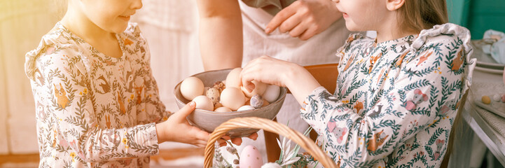 Wall Mural - happy easter holiday time in spring season. family mother and little kids girls decorate a wicker basket with eggs and baked cakes. festive home decor. traditional food. banner. flare