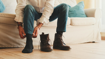 Close-up of legs of mature man putting on casual boots, tying shoelaces