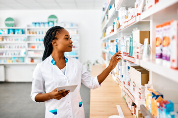 Wall Mural - Young black pharmacist using touchpad while working in drugstore.