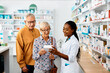 © Drazen - Young black pharmacist assists senior couple in buying medicine in drugstore.