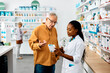 © Drazen - African American female pharmacist advising senior man in pharmacy.
