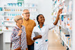 © Drazen - Happy African American female pharmacist assists senior couple who is buying medicine in drugstore.