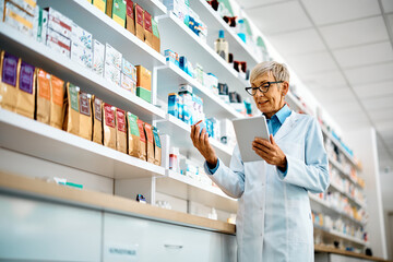 Wall Mural - Senior pharmacist using touchpad while examining medicine in pharmacy.