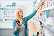 © Drazen - Mid adult woman looking for medicine on shelf in pharmacy.